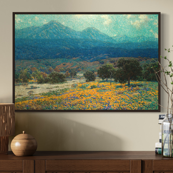 Framed landscape painting of a mountainous landscape with fields of flowers on a wall above a wooden console table.